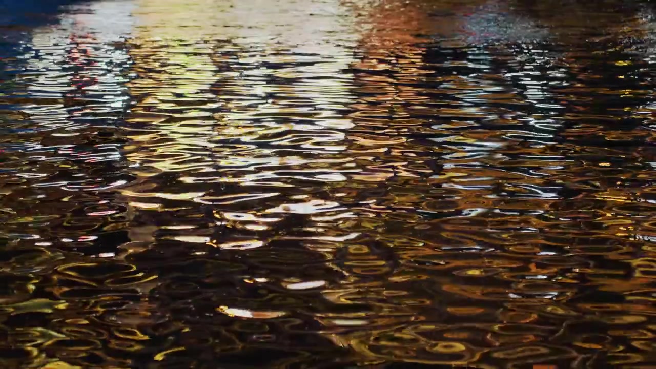 Night water reflecting city lights, rippling. Golden shimmer across surface, neon bokeh from street lamps, wet pavement echo, calm ambient mood, ideal for urban night walking sequences, cinematic