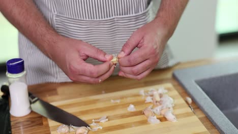 close-up of hands peeling garlic cloves on a wooden cutting board
