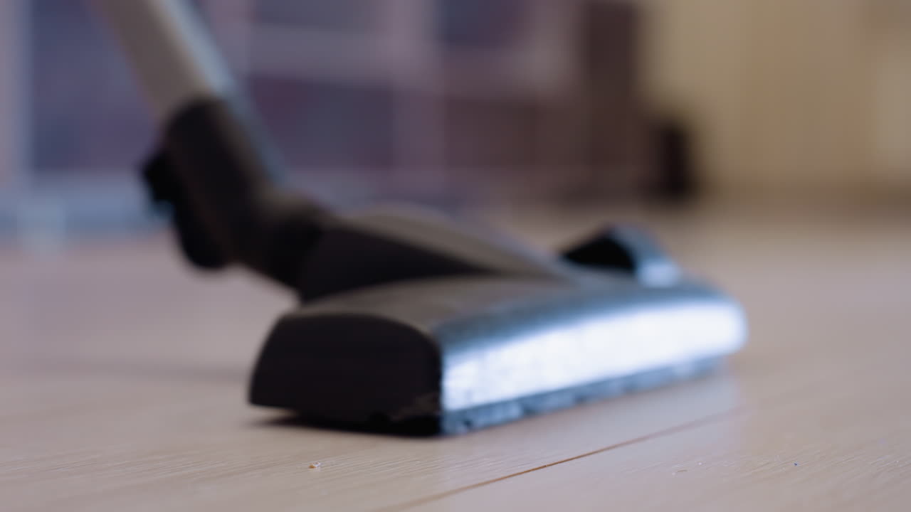 Close up of vacuum cleaner head moving forward and backward across light wooden floor removing dust and dirt, representing daily household cleaning activity, hygiene, and modern home maintenance