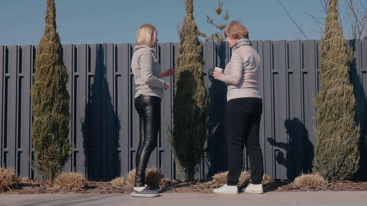 회색 울타리 와 식물 근처 에 있는 야외 에서 이야기 하는 두 여자