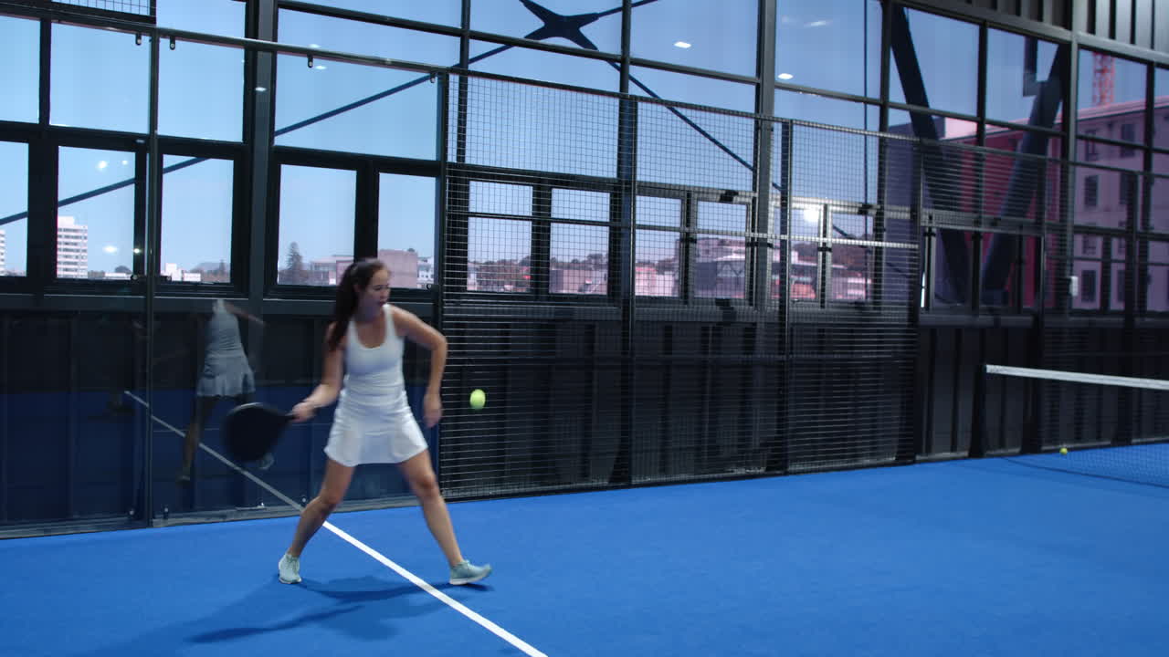 Man playing padel tennis on indoor court, hitting ball with racket energetically