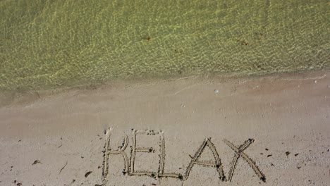 camera tilts down from the horizon showing the sea to relax written in the sand on a beach