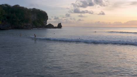 Toma-Cinematográfica-De-Personas-Relajándose-En-El-Agua-Y-Surfeando-En-Una-Playa-Exótica-Durante-La-Puesta-De-Sol-Y-La-Hora-Dorada