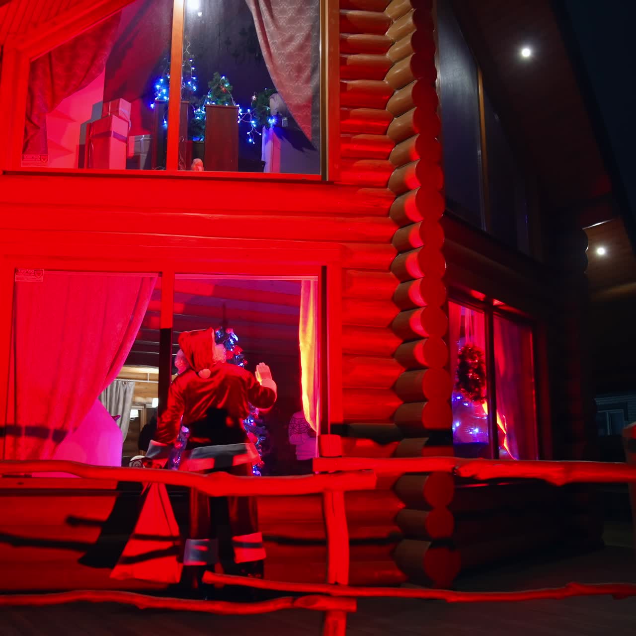 Santa near beautiful decorated house at Christmas night. Santa Claus in red costume coming to the house and looking inside through window