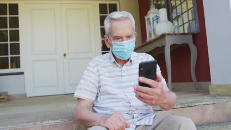 Hombre-Caucásico-Mayor-Con-Mascarilla-Usando-Un-Teléfono-Inteligente-Para-Video-Chat