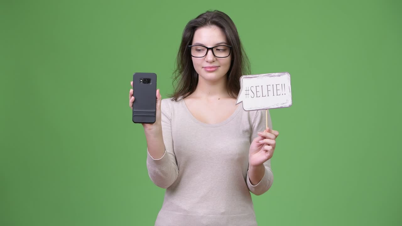 Young happy beautiful woman holding phone and selfie paper sign