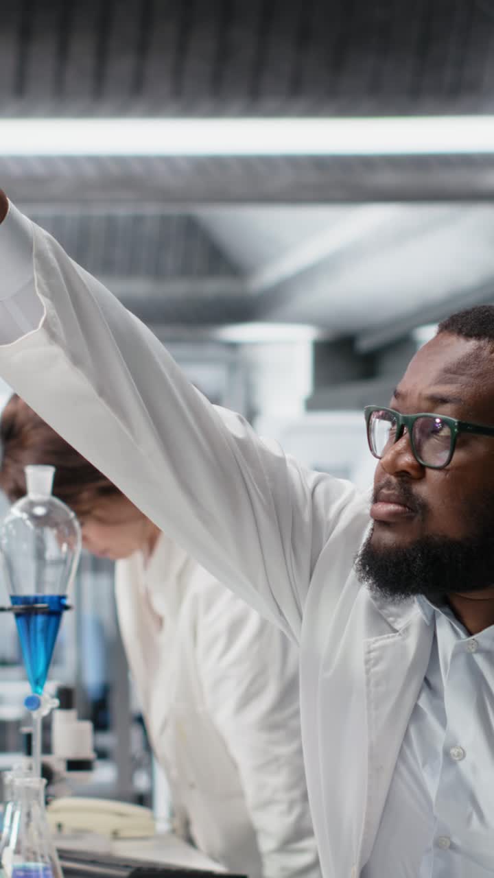 Vertical video Clinical microbiologist in lab looking at blood sample in test tube, using PC