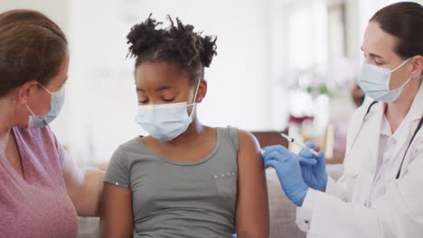 African-american-girl-with-caucasian-mother-and-female-doctor-wearing-face-masks,-vaccinating