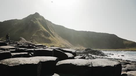 Tourist-walking-on-Giant's-Causeway-in-front-of-mountainous-scenery