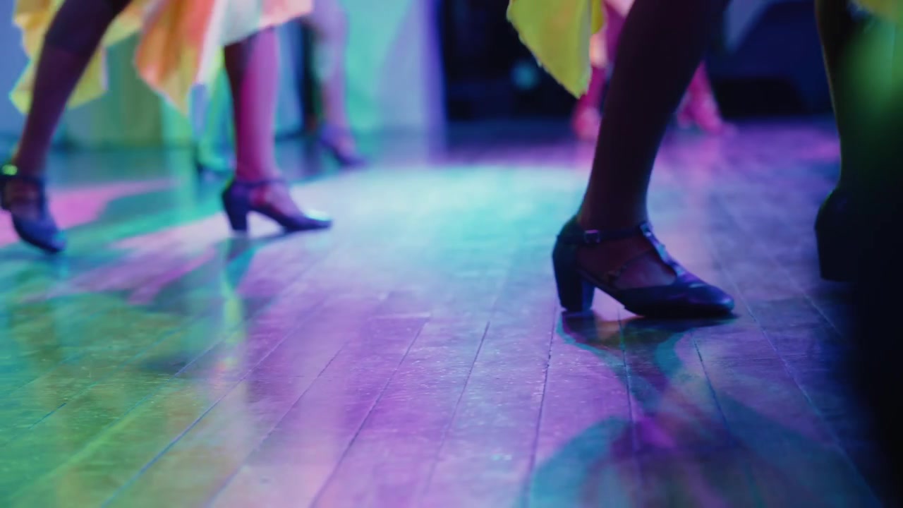 Nærbillede fra lav vinkel af danseres ben og fødder i bevægelse på et blankt gulv.