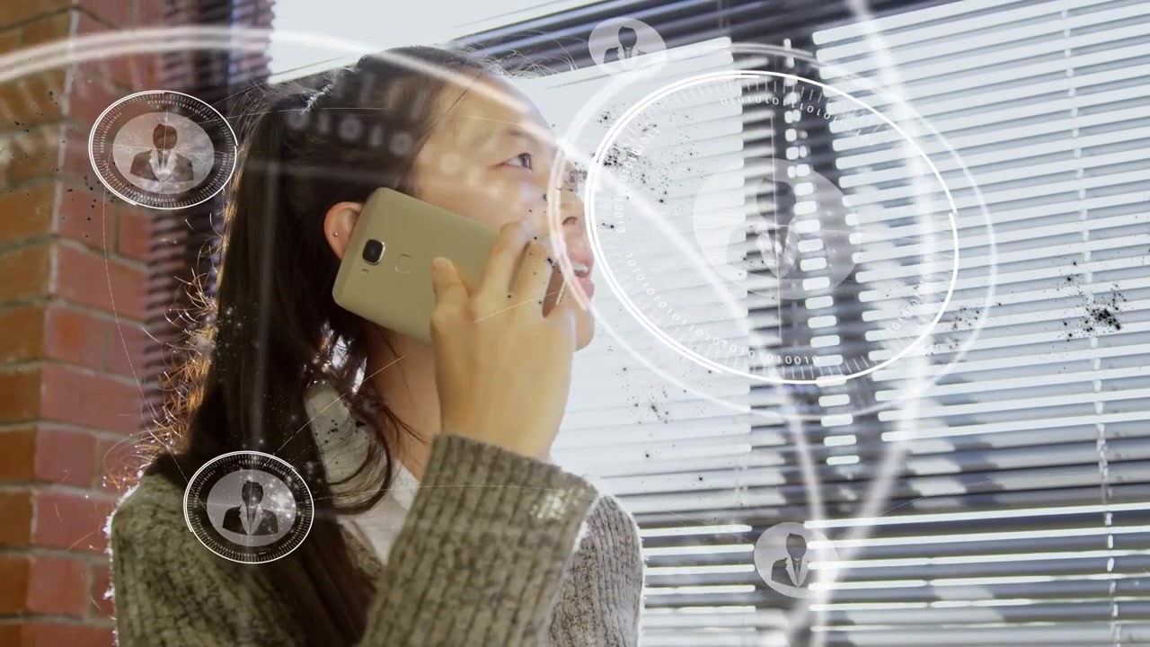 グレーのセーターを着たアジア人女性がロフトで電話を受け、仕事の通話を続けている。HUDが拡大表示される。
