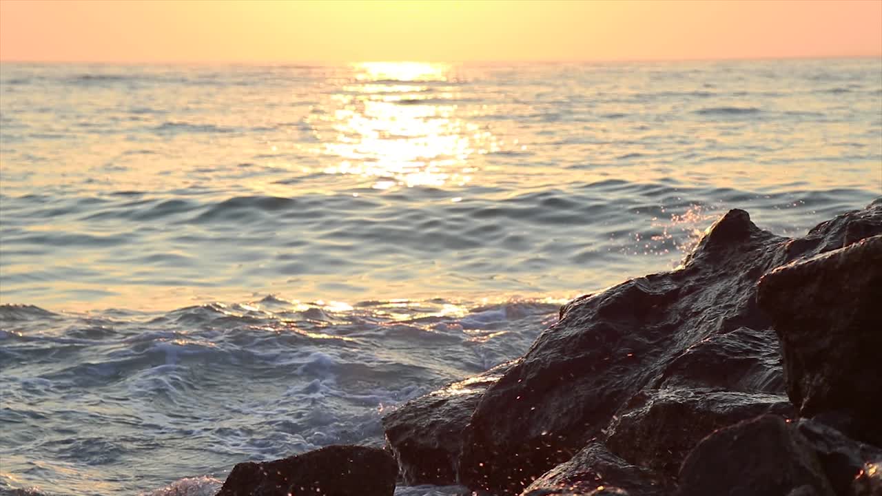 Ondas quebrando nas rochas de uma praia rochosa ao pôr do sol