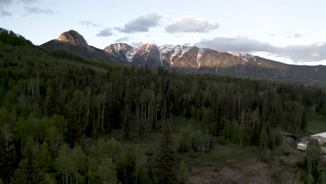 colorado rocky mountains with forest clearing and logging mill, aerial flyover shot