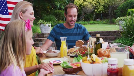 Lächelnde-Kaukasische-Familie,-Die-Händchen-Hält-Und-Vor-Dem-Gemeinsamen-Festessen-Im-Garten-Gnade-Sagt