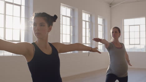 yoga-class-of-healthy-pregnant-women-practicing-warrior-pose-enjoying-group-physical-fitness-workout-with-instructor-in-studio-at-sunrise