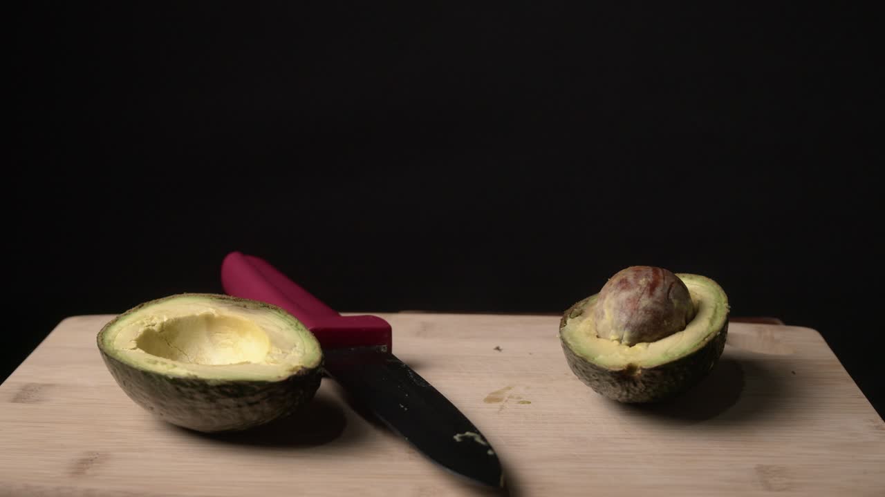A halved avocado on a rustic wooden table under soft, moody lighting. The scene emphasizes the fruit’s rich green color and creamy texture, perfect for themes of healthy eating and organic food