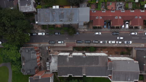 Aerial-birds-eye-overhead-top-down-panning-view-of-street-in-urban-neighbourhood.-Car-driving-between-cars-parked-along-road.-London,-UK