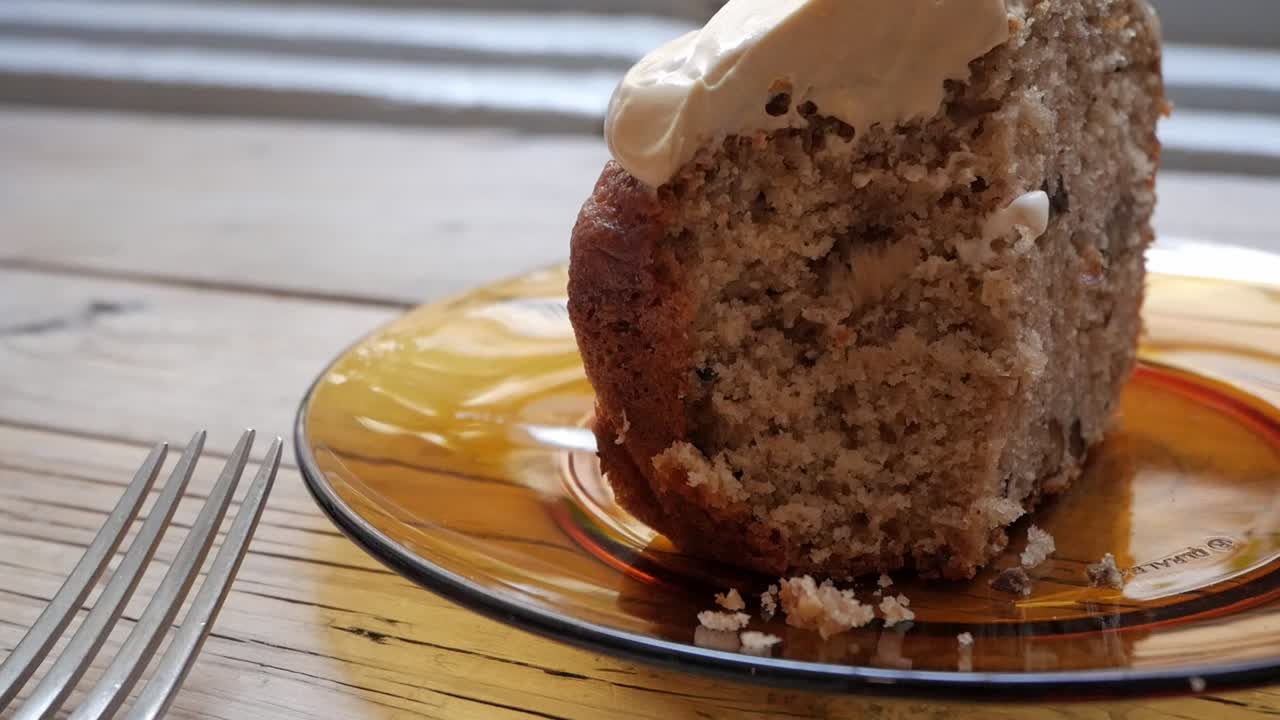 A fork spreading creamy frosting on a slice of freshly baked carrot cake on a plate