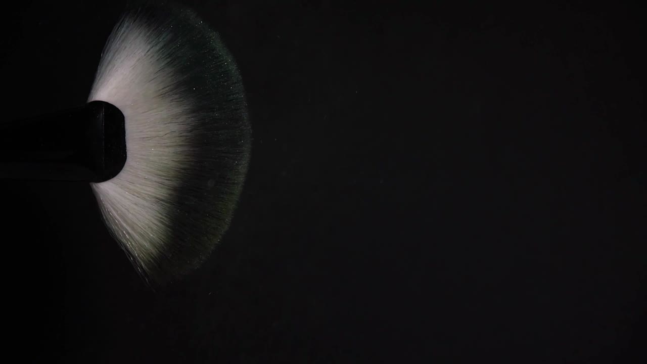 cámara lenta de un pincel de maquillaje con explosión de polvo amarillo y explosión en fondo negro