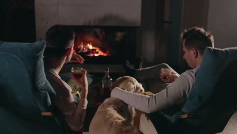 two men relaxing by a fireplace with a dog