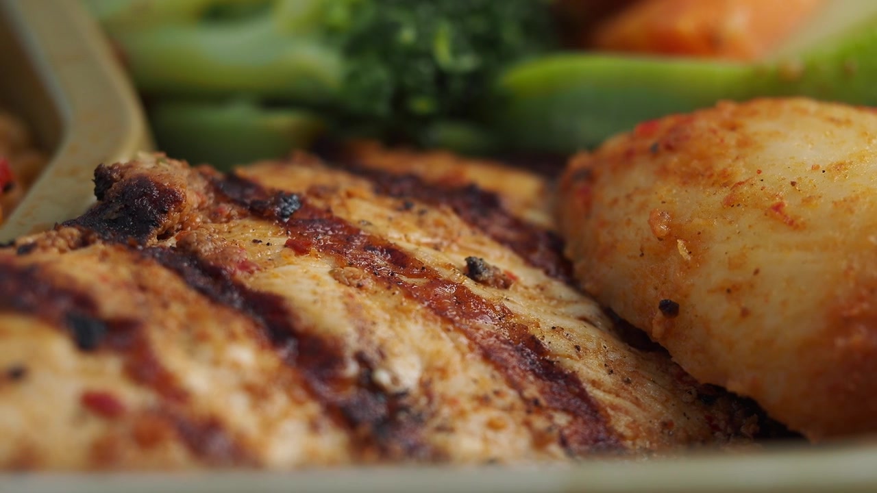 Primo piano di pollo alla griglia con verdure e cereali.