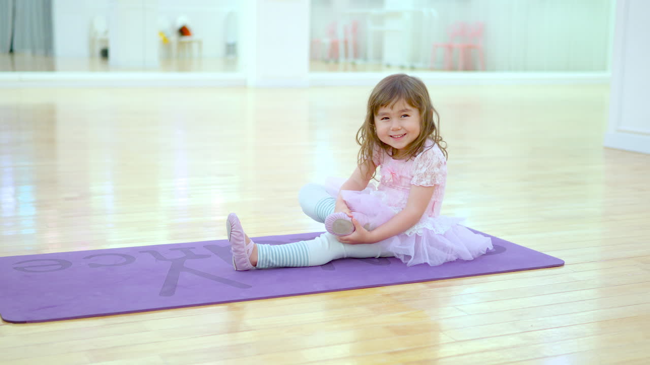 Pretty Little Ballerina in a Pink Tutu Dress Stretches Legs in Empty Ballet Studio Smiling