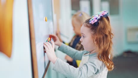 little girls near the board with magnets in primary school. children playing with colorful magnets on white board on the background of classroom.