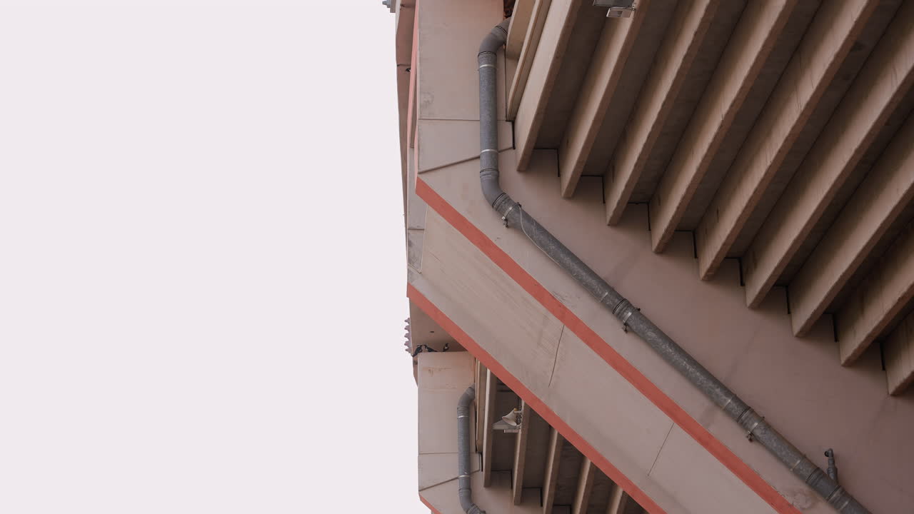 Varandas de concreto diagonais com nervuras repetitivas, vista em close-up de fachada urbana e cano enferrujado, geometria modernista projetando sombras dramáticas em reboco fosco, atmosfera arquitetônica austera.