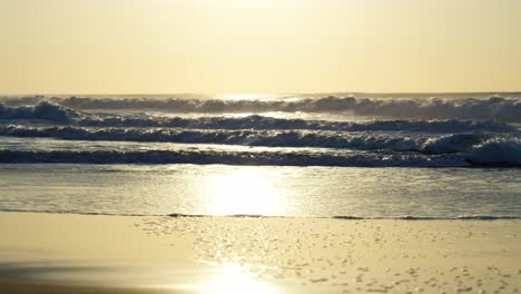 A golden glow illuminates the scene as waves rush to shore, adding depth to this dramatic coastal view.