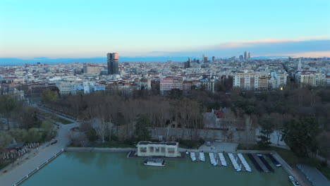 drone footage flying backwards over a vibrant urban scene in madrid. the clip reveals retiro lake and lush park surroundings with early morning light and detailed architecture