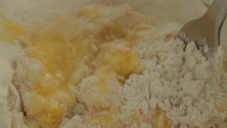 macro shot mixing eggs into flour with fork