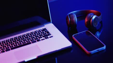 video of laptop, smartphone and headphones on desk with copy space on neon background