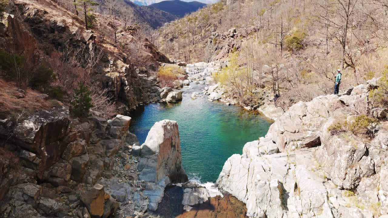 Praglia river gorge, Italy, turquoise pool, cascades, rocky canyon with lone hiker, ideal for adventure, nature, travel. Aerial top-down backward, tilt-up reveal