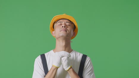 close up of asian man painter wearing safety helmet praying for something while standing in the green screen background studio