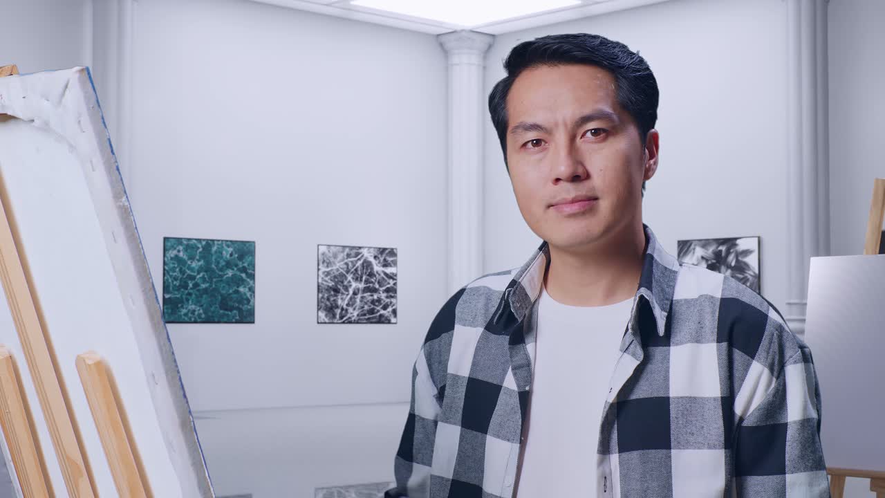 갤러리에서 오일 페인트와 으로 캔버스에 그림을 그리는 동안 머리를 흔들고 엄지손가락을 보여주는 아시아 남성 예술가의 클로즈업
