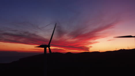 aerial close up silhouette of rotating windmill turbines, producing green energy outdoors during beautiful sunset in the evening