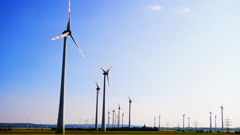 Turbines on a sunny day. Rows of wind turbines spin slowly under a clear blue sky in a rural landscape, showcasing renewable energy in action