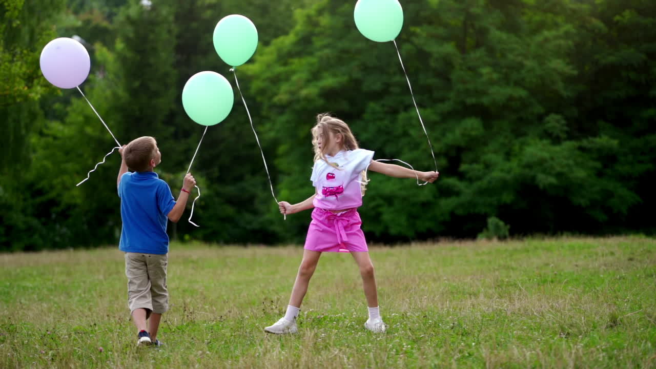 Boy and girl are playing with baloons outside. Happy children jump on grass in summer. Family day on weekend. Happiness concept.