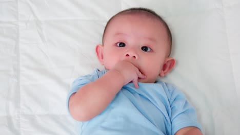 happy family, cute asian newborn baby wear blue shirt lying play on white bed looking at camera with laughing smile happy face. innocent little new infant adorable. parenthood and mother day concept.