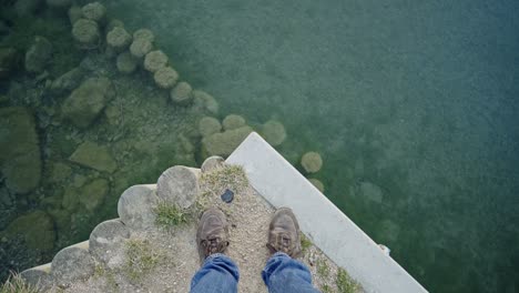 Male-feet-in-jeans-and-shoes-with-ties-standing-at-edge-of-lake,-high-angle-shot