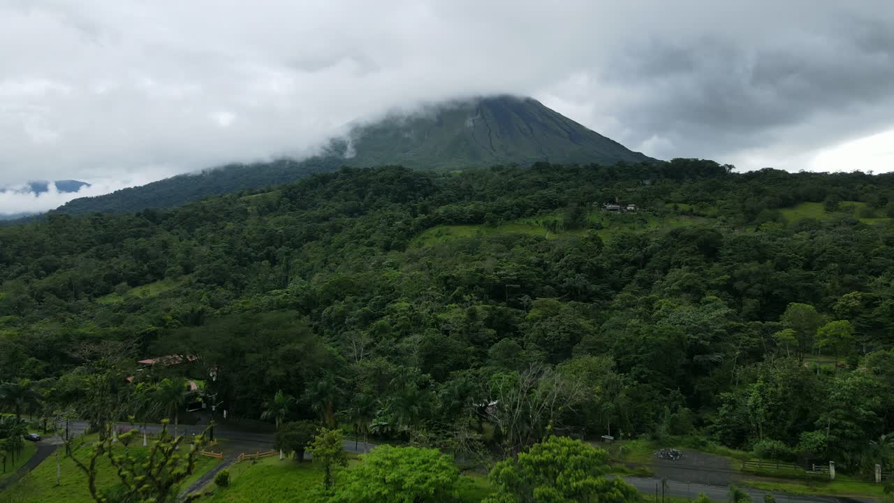 vista aérea en movimiento hacia adelante, carretera en las estribaciones del volcán arena en costa rica, vista panorámica de árboles y cielo nublado en el fondo