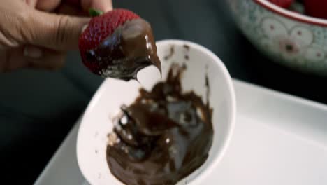 dipping strawberries in melted chocolate fondue inside a white dish for valentine's day