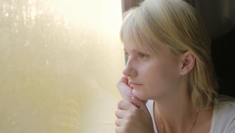 Portrait-Of-A-Young-Woman-Traveling-In-A-Train-Looking-Out-The-Window-The-Sun's-Rays-Illuminate-Her-