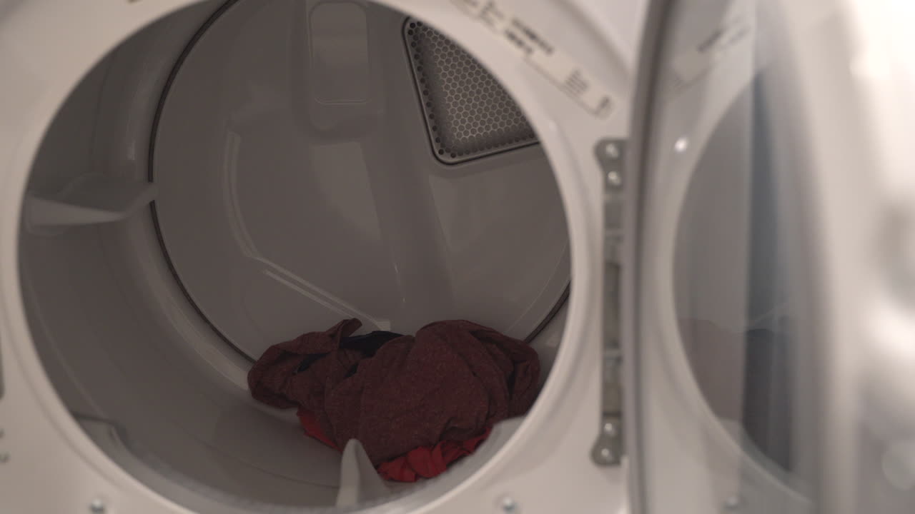 Close up of a man loading clothes into a dryer from the washing machine next to it