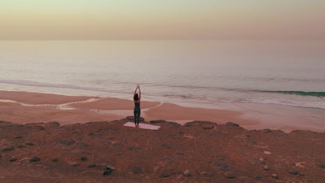 woman practicing yoga on a beach at sunrise