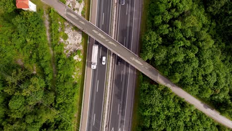 disparo de avión no tripulado de arriba hacia abajo de una carretera europea ligeramente húmeda con paso elevado y líneas eléctricas que la atraviesan y árboles que rodean la carretera nacional