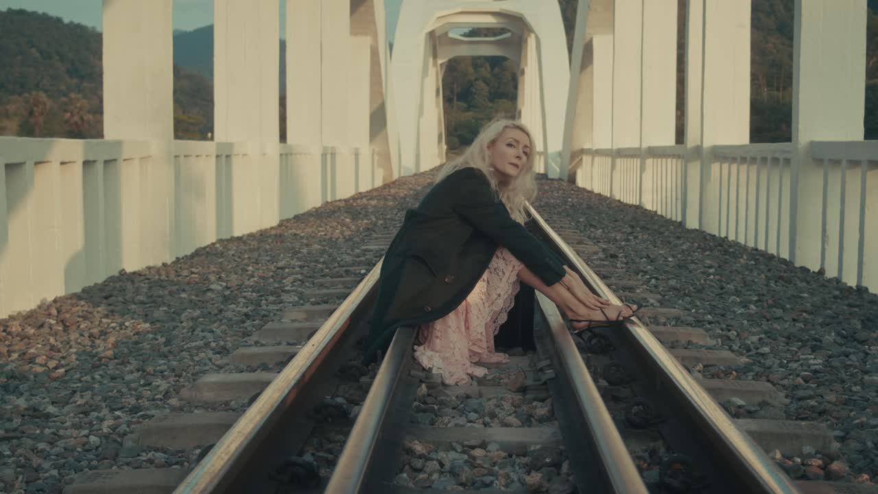 Woman Sitting on Railroad Tracks on a Bridge