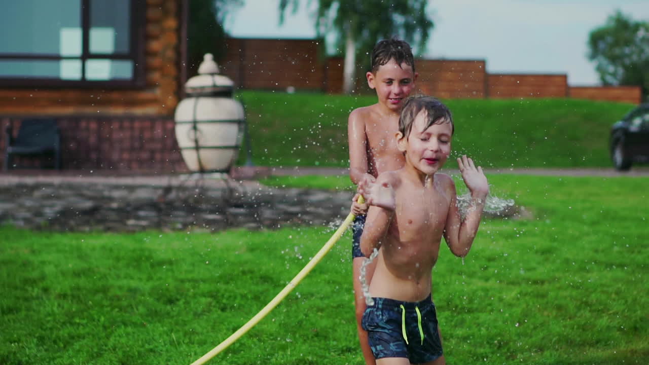 아버지 와 두 자녀 와 함께 잔디 ⁇  에서 놀면서 물 을  ⁇ 고 웃고 놀이터 에서 재미 를 즐기고 있으며, 호수 근처 에 있는 집 의 배경 에 잔디 ⁇  이 있다