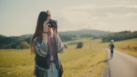 young woman clicking pictures through camera near meadow