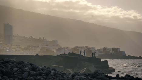 men standing over the rocks at the shore just along the ocean, under a cloudy sky. slow motion.